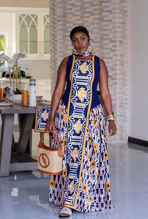 A bold geometric Tshwane print maxi dress featuring a fitted sleeveless bodice in navy with mustard accents and a flared skirt with intricate patterns in earthy tones. The dress combines structured elegance with flowing gathers, perfect for a statement look.