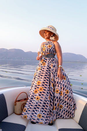 Elegant halter-neck maxi dress featuring the vibrant Tshwane Sunflower print in mustard and navy tones, with a cinched waist and flowing silhouette.