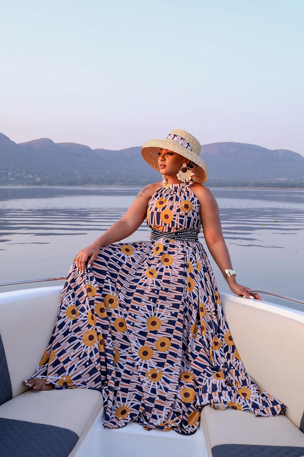 Elegant halter-neck maxi dress featuring the vibrant Tshwane Sunflower print in mustard and navy tones, with a cinched waist and flowing silhouette.